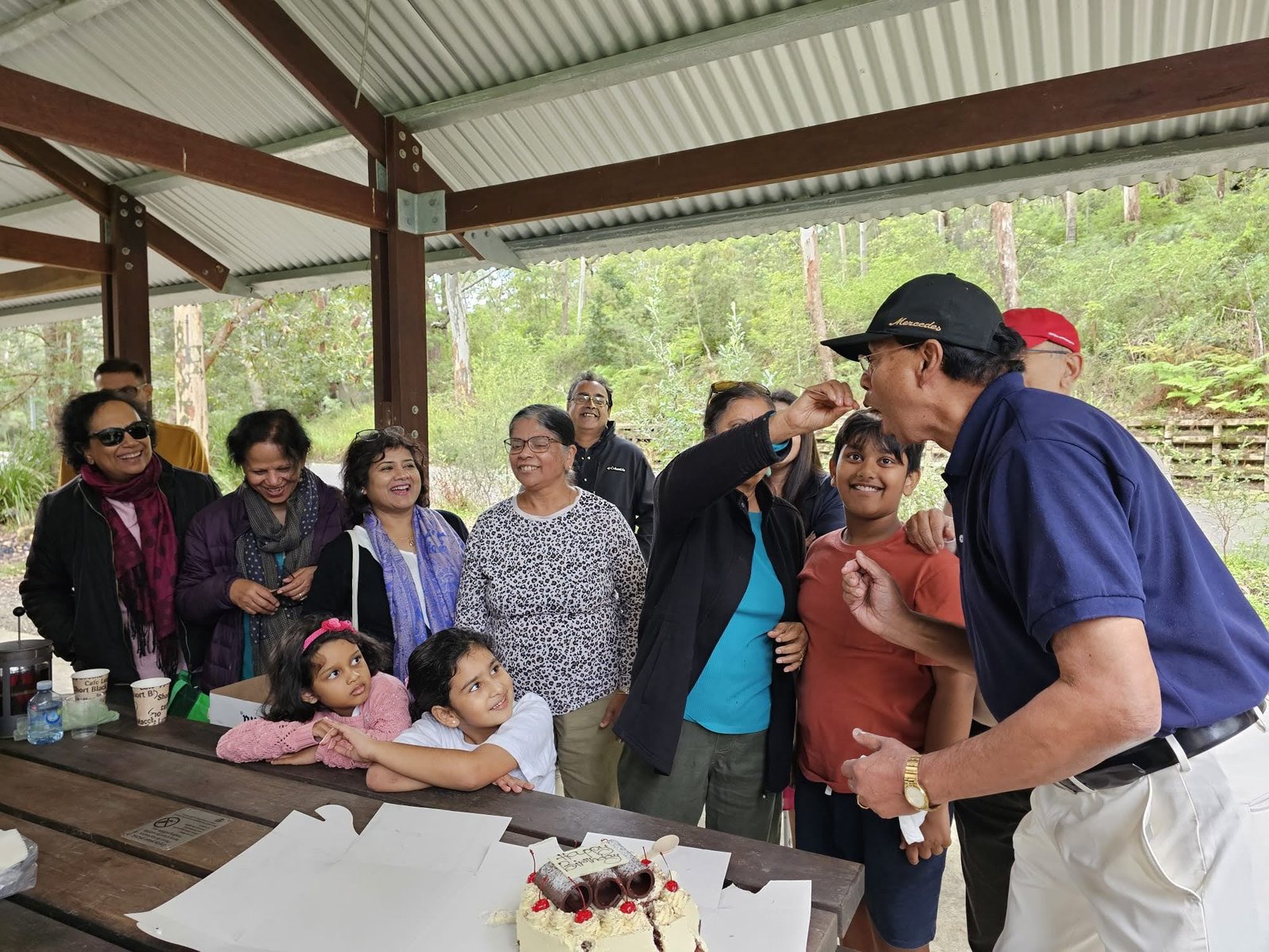 Home Alumni and children gathered around a birthday cake at a bush picnic shelter